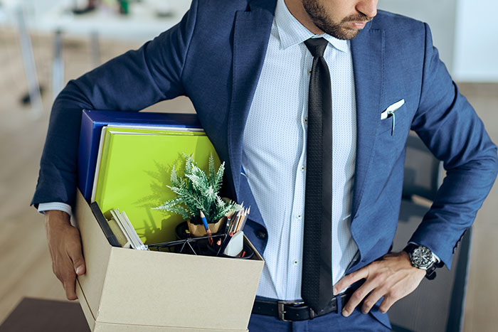 Businessman holding a box of personal items, showing consequences of a boss threatening employee with termination. Businessman holding a box of personal items, showing consequences of a boss threatening employee with termination.