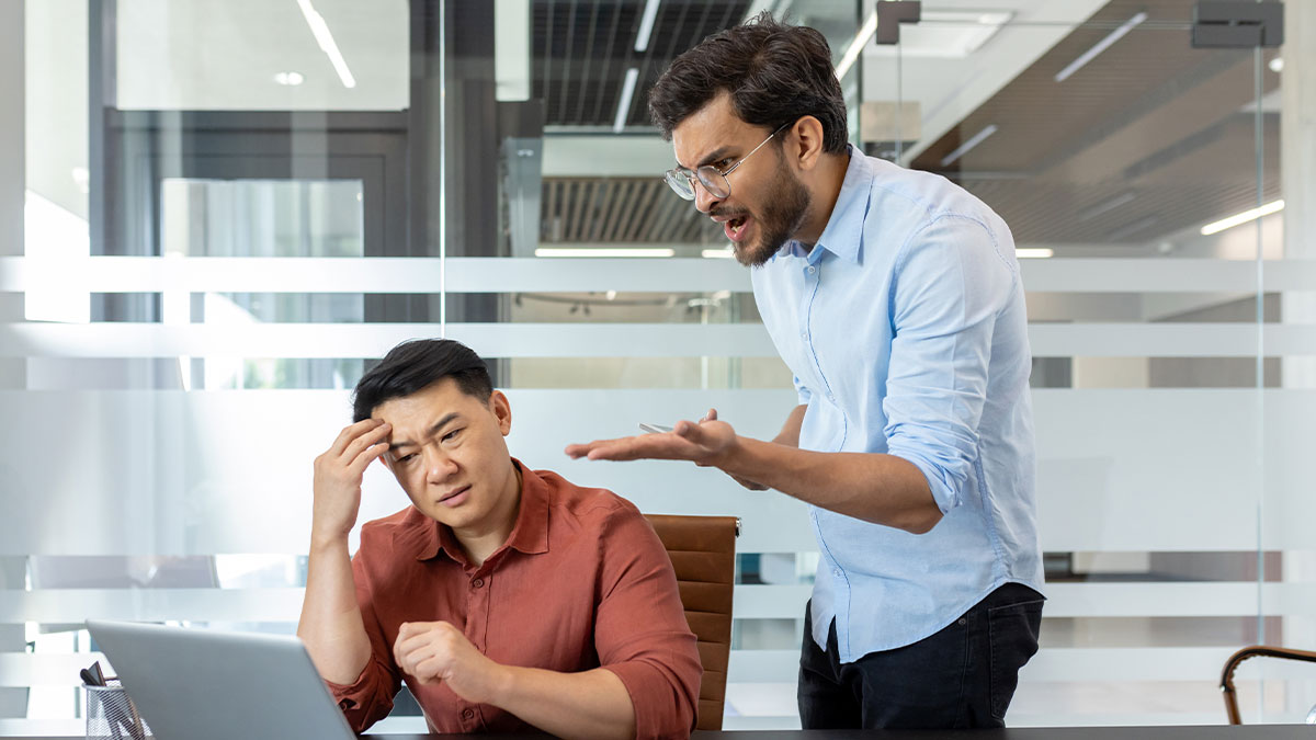 Angry boss threatening stressed employee at desk in modern office, illustrating boss keeps threatening employee with termination.