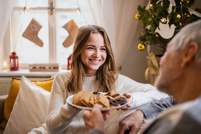 Woman smiling and offering a plate of cookies during Christmas, calling out men who feel entitled to do nothing. Woman smiling and offering a plate of cookies during Christmas, calling out men who feel entitled to do nothing.