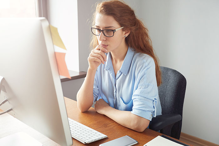 Woman with glasses thoughtfully using computer at desk, representing entitled mother expenses split with son and girlfriend. Woman with glasses thoughtfully using computer at desk, representing entitled mother expenses split with son and girlfriend.