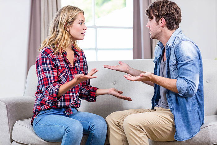 Young couple arguing on a couch about entitled mother expenses split with son's girlfriend in a bright living room. Young couple arguing on a couch about entitled mother expenses split with son's girlfriend in a bright living room.
