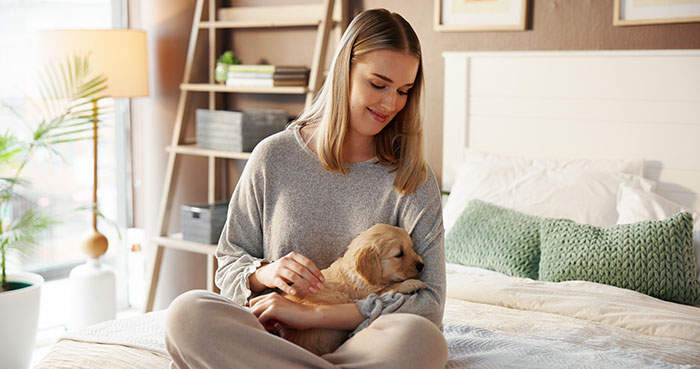 Young woman sitting on bed, smiling while holding a puppy, highlighting entitled mother expenses and split family themes. Young woman sitting on bed, smiling while holding a puppy, highlighting entitled mother expenses and split family themes.