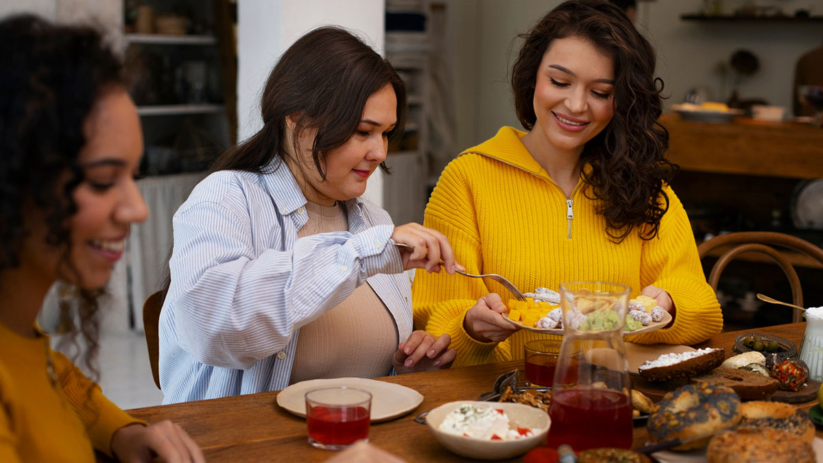Three women enjoying Thanksgiving dinner together with plates of food and drinks on the table, focusing on leftovers.