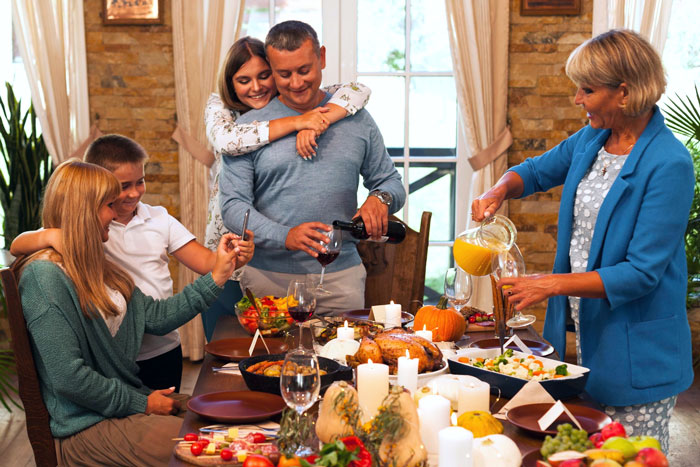 Family enjoying Thanksgiving dinner together with food and drinks on the table in a warm, cozy dining room setting.