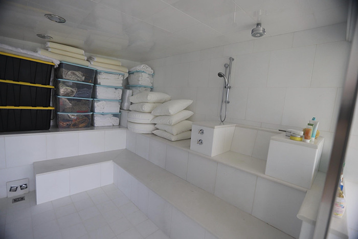 Sterile tiled bathroom inside Epstein’s private island home with shower and stacked pillows and storage containers. Sterile tiled bathroom inside Epstein’s private island home with shower and stacked pillows and storage containers.