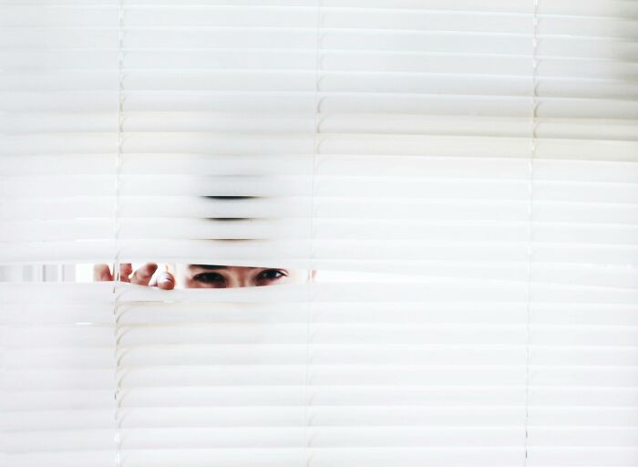 Person peeking through white blinds, symbolizing moral compass being tested with challenging shocking dilemmas.
