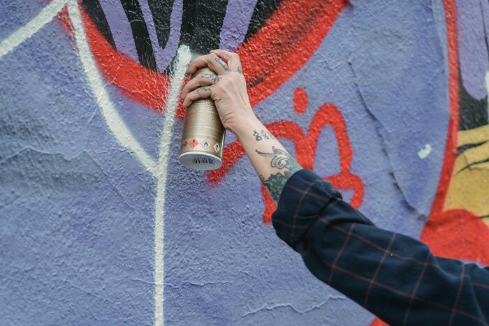 Hand with tattoos holding a spray paint can, creating street art on a colorful wall, testing your moral compass visually.