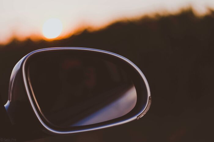 Car side mirror reflecting sunset and blurred landscape, symbolizing moral compass and ethical dilemmas ahead.
