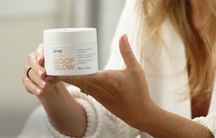 Person holding a jar of goop beauty GOOP GLOW hair mask, highlighting product packaging and label details.
