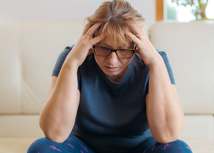 Woman wearing glasses, holding her head in distress, illustrating people sharing the moment they realized they are in a cult.