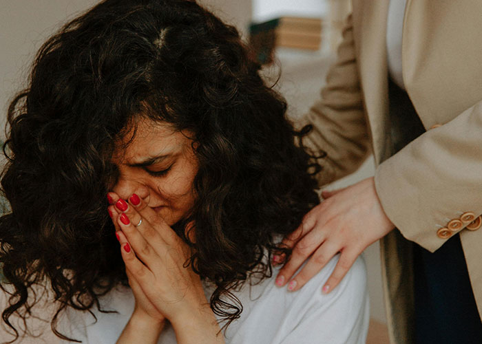 Woman with curly hair looking distressed while another person comforts her, capturing the moment they realize they are in a cult.