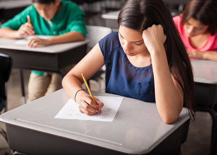 Teen girl writing at desk in classroom, appearing concerned, illustrating the moment they realized they are actually in a cult.