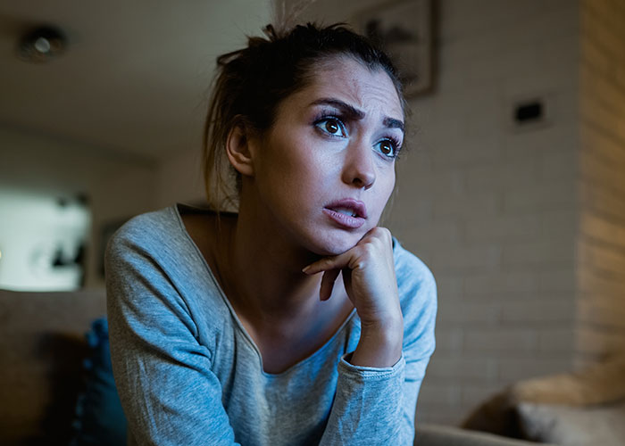 Woman with worried expression sitting indoors, reflecting on her experience with a real cult group.