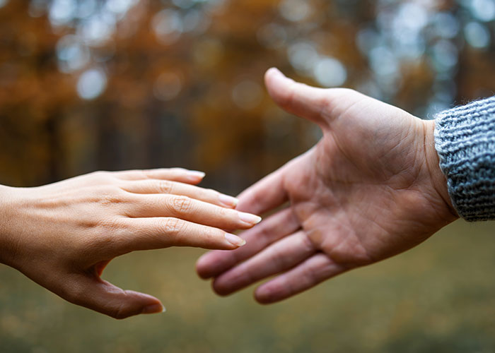 Two hands reaching out to each other outdoors, symbolizing connection and trust in former cult members' experiences.