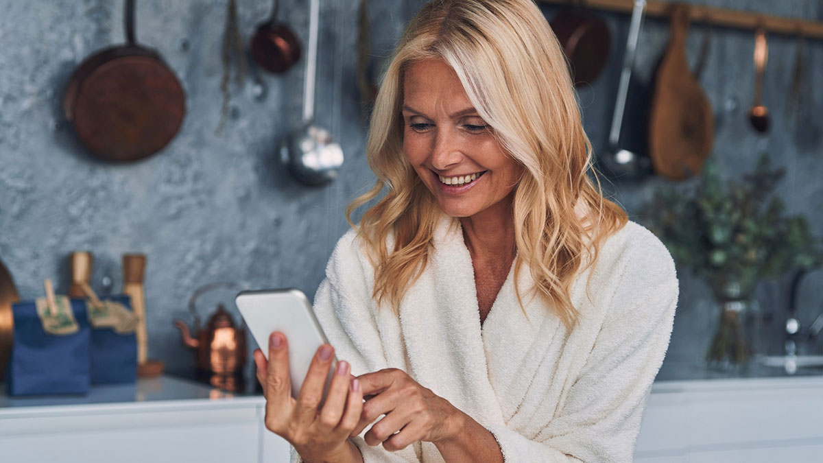 Woman in a white robe smiling while looking at her smartphone, representing crazy things people do to make their ex pine.