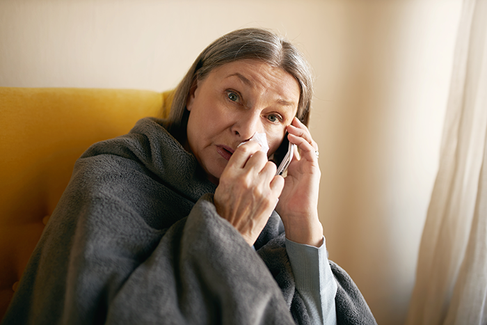 Older woman wrapped in blanket, wiping tears while talking on phone, reflecting upset feelings about baked potato disagreement.