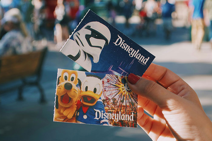 Hand holding Disneyland tickets featuring Star Wars and classic characters in a crowded park setting. Hand holding Disneyland tickets featuring Star Wars and classic characters in a crowded park setting.