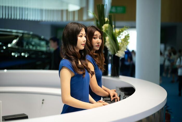 Two women in blue dresses standing behind a modern curved desk, representing examples of instant karma in action.