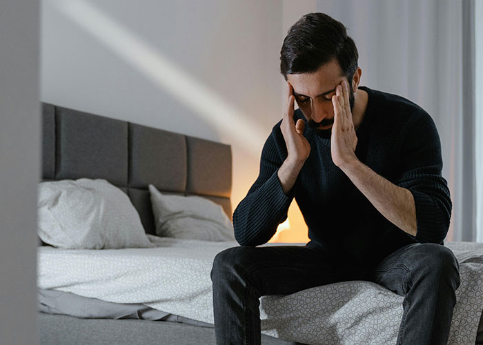 Man sitting on edge of bed holding his head, appearing stressed and overwhelmed by fiancée’s unexpected wedding request. Man sitting on edge of bed holding his head, appearing stressed and overwhelmed by fiancée’s unexpected wedding request.