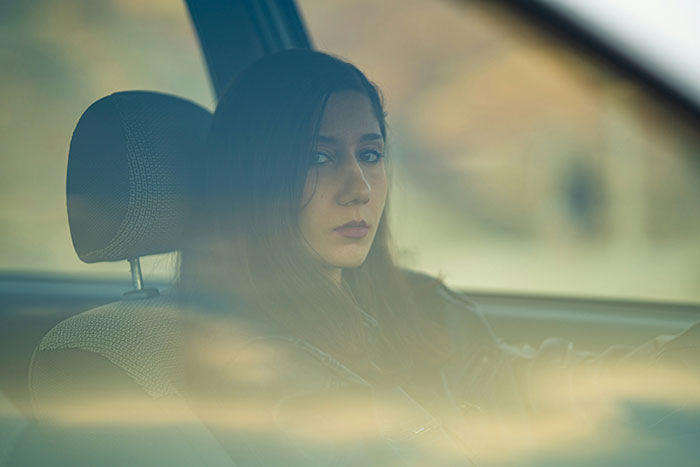 Woman in car looking serious through window, representing a girlfriend overhearing a shameless guy flirting with baby mama.