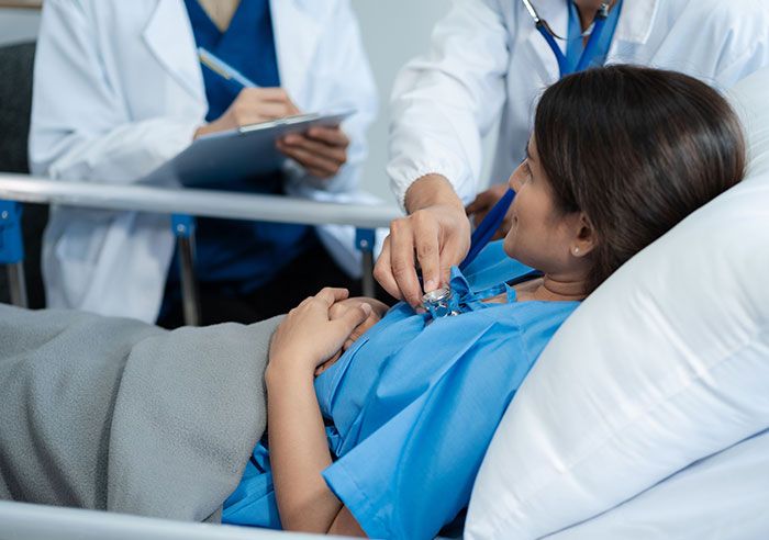 Woman in hospital bed being examined by doctor with stethoscope, highlighting distress in long-term marriage and restraining order issues.
