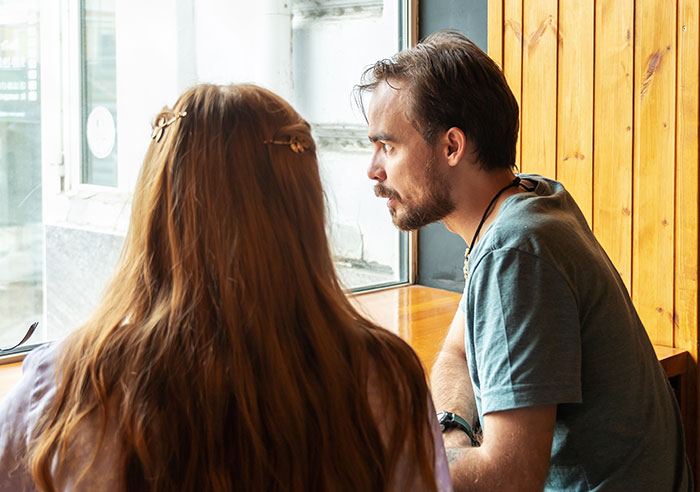 Couple having a serious conversation by the window in a wooden cafe, reflecting on restraining order issues with MIL.