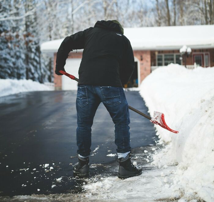 Postal worker shoveling snow during winter to keep pathways clear while delivering mail in a residential neighborhood.