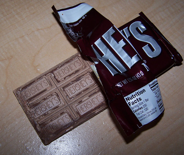 Partially unwrapped Hershey's chocolate bar on a wooden surface highlighting food safety facts related to packaged snacks.