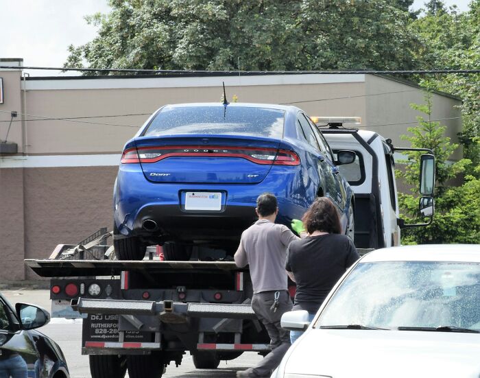 Blue Dodge GT being towed on a flatbed truck illustrating instant karma after a parking violation.