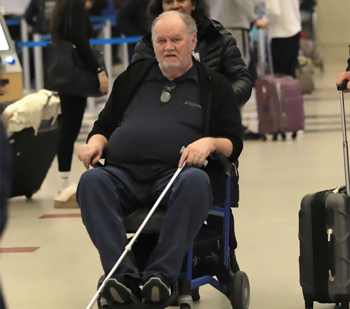 Elderly man in wheelchair holding a cane, surrounded by travelers at a busy airport terminal. Elderly man in wheelchair holding a cane, surrounded by travelers at a busy airport terminal.