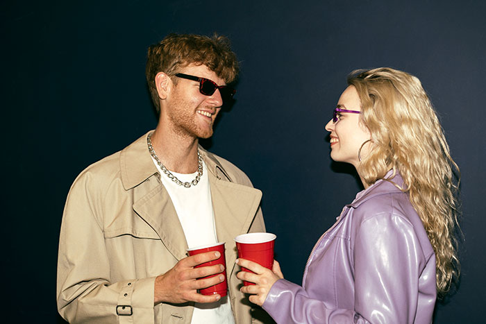 Young girl and friend laughing and roasting each other with playful insults while holding red cups at a party Young girl and friend laughing and roasting each other with playful insults while holding red cups at a party