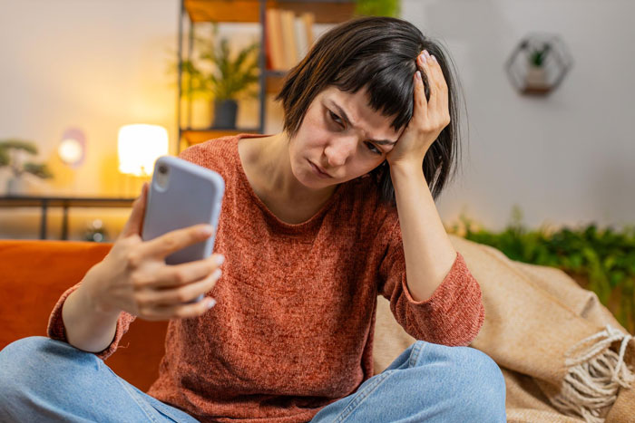 Young woman in a sweater looking frustrated while holding a phone, depicting ghosting after getting a boyfriend. Young woman in a sweater looking frustrated while holding a phone, depicting ghosting after getting a boyfriend.