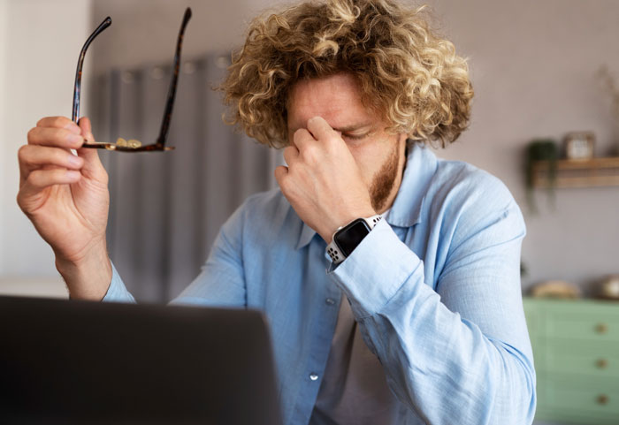 Man frustrated at laptop, holding glasses, symbolizing writer struggling to break into Hollywood industry. Man frustrated at laptop, holding glasses, symbolizing writer struggling to break into Hollywood industry.
