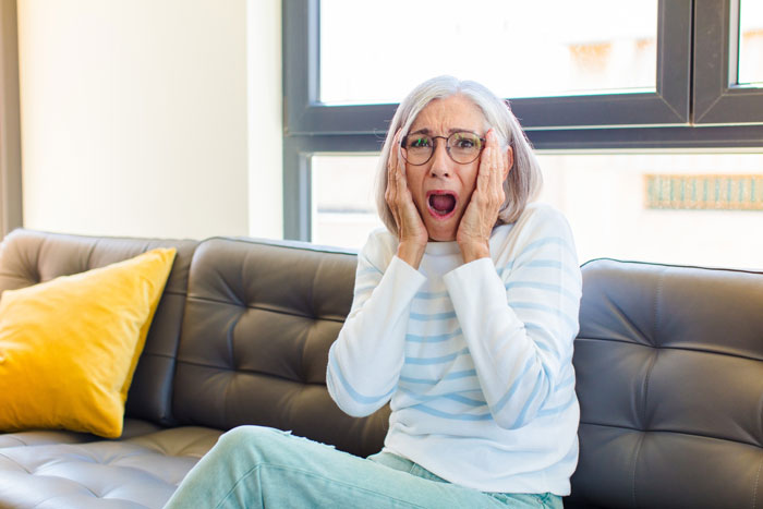 Elderly woman sitting on couch looking shocked and worried after guy’s hometown blows up his phone about funeral wishes. Elderly woman sitting on couch looking shocked and worried after guy’s hometown blows up his phone about funeral wishes.