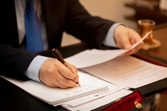 Man in suit writing notes on paper while holding documents, illustrating communication about funeral wishes and hometown reaction. Man in suit writing notes on paper while holding documents, illustrating communication about funeral wishes and hometown reaction.