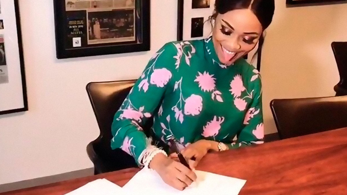 Woman in a floral green top happily writing at a wooden desk, capturing college memes for students running on hope and energy drinks.