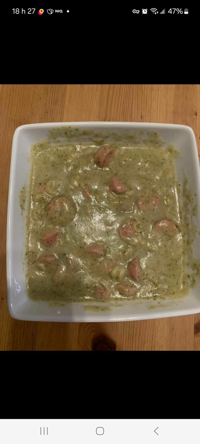 Bland looking green soup with chunks of sausage in a white bowl on a wooden table, food pics to be shamed.