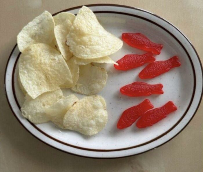 Potato chips and red fish-shaped gummy candies served together on a plate in a food pic to be shamed online