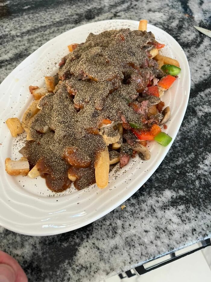 Plate of fries covered in brown gravy, vegetables, and an excessive amount of black pepper, a food pic to be shamed online