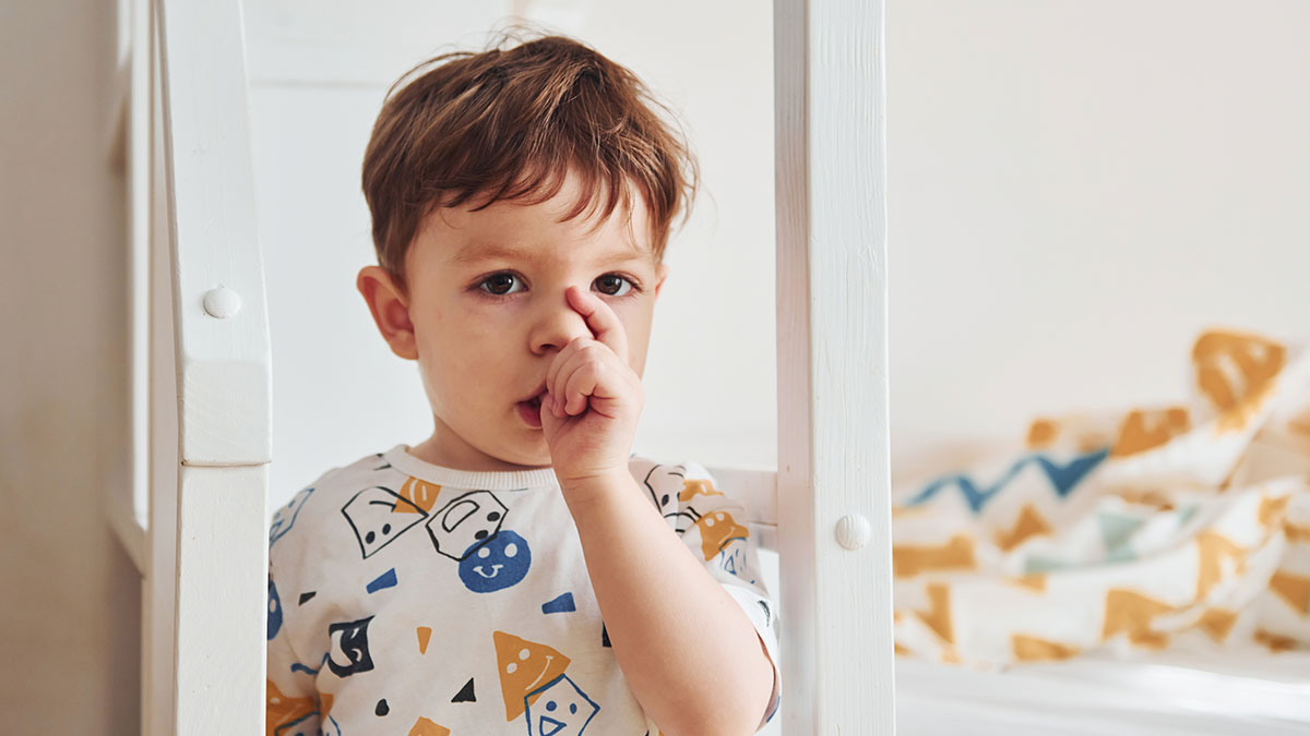 Toddler picking nose indoors wearing fun patterned shirt, capturing funny moments parents post during quiet time.