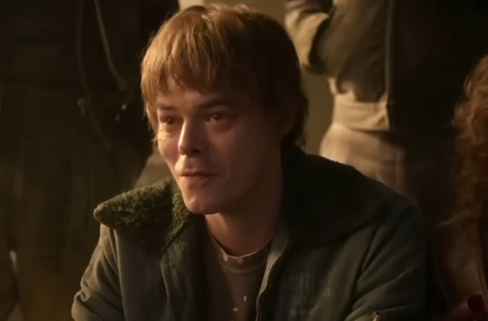 Young man with light brown hair wearing a green jacket, captured in a dimly lit scene from Stranger Things Season 5.
