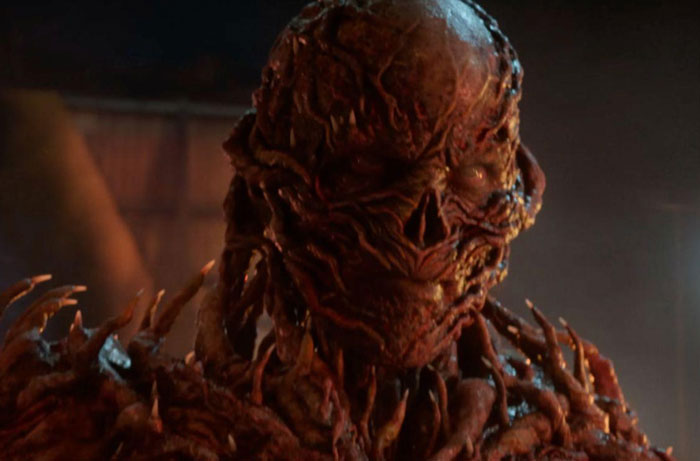 Close-up of a terrifying creature from Stranger Things with detailed horror makeup and textured skin in a dark scene.