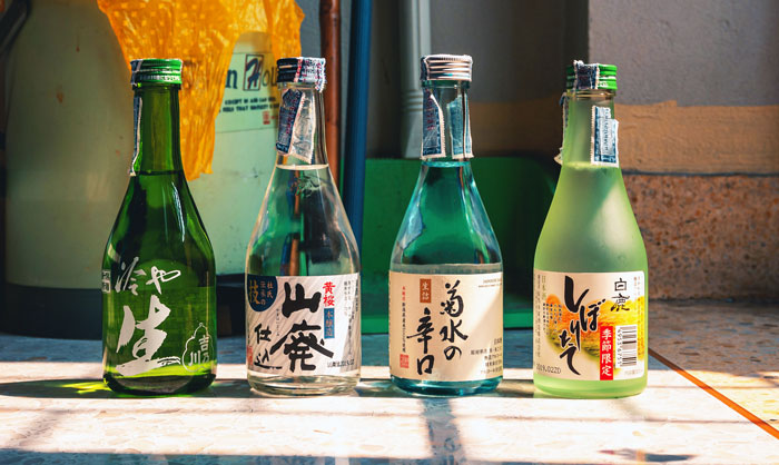 Four souvenir wine bottles from abroad lined up on a sunlit surface, showcasing their unique labels and designs. Four souvenir wine bottles from abroad lined up on a sunlit surface, showcasing their unique labels and designs.