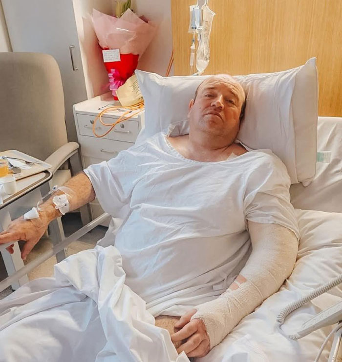 Man with bandaged arm lying in hospital bed recovering after Bondi Beach attack, relating to swimwear model controversy. Man with bandaged arm lying in hospital bed recovering after Bondi Beach attack, relating to swimwear model controversy.