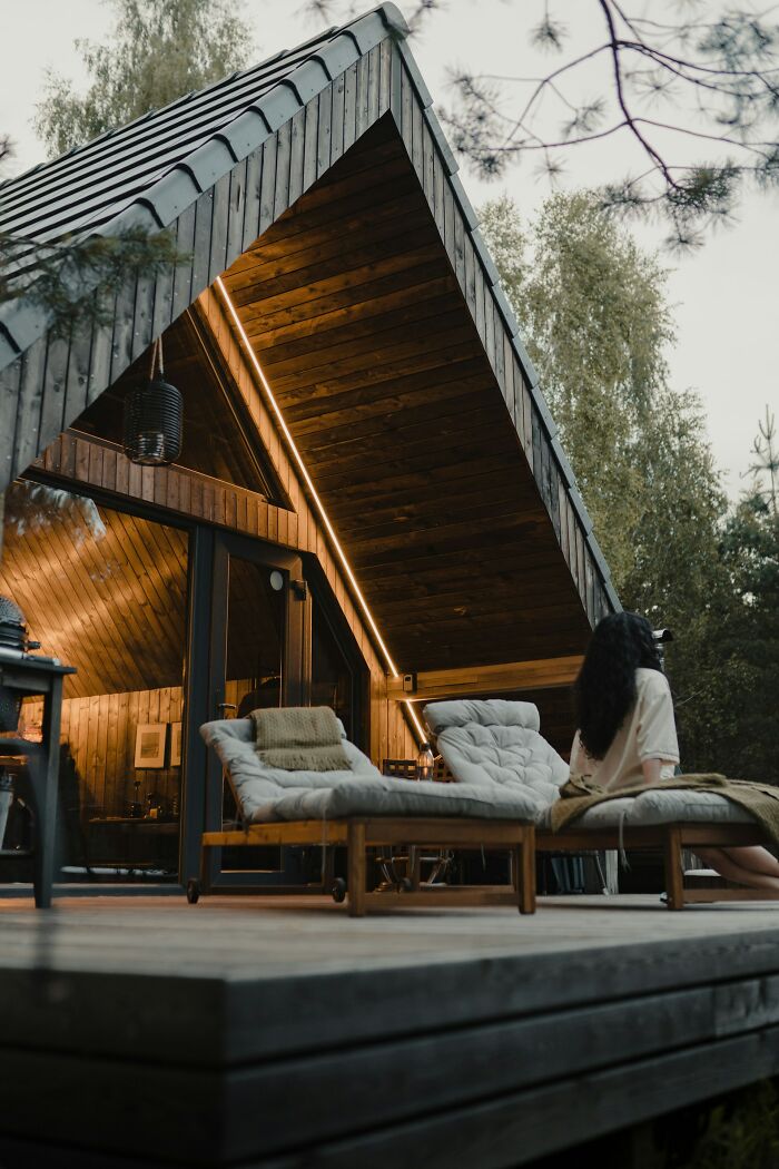 Modern wooden cabin exterior with cozy lounge chairs on patio, nature surroundings, showcasing incredible minds and genius creativity.