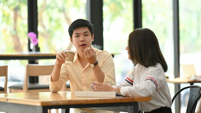 Two young adults talking at a cafe, showing signs of still stuck in their high school era years later.