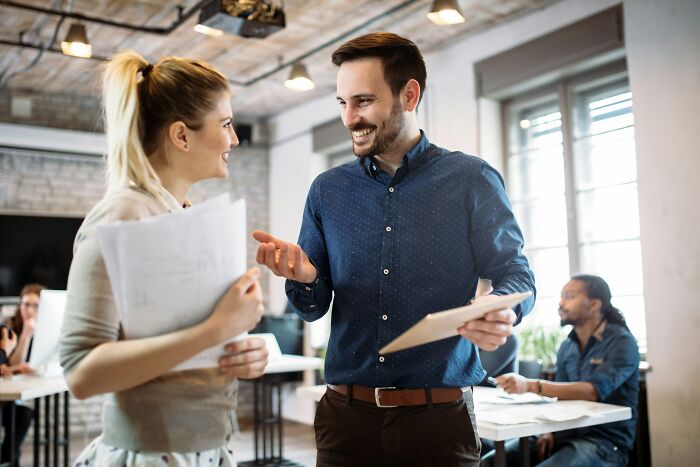 Two coworkers smiling and discussing papers in a modern office, illustrating bizarre and unbelievable baby names concept.