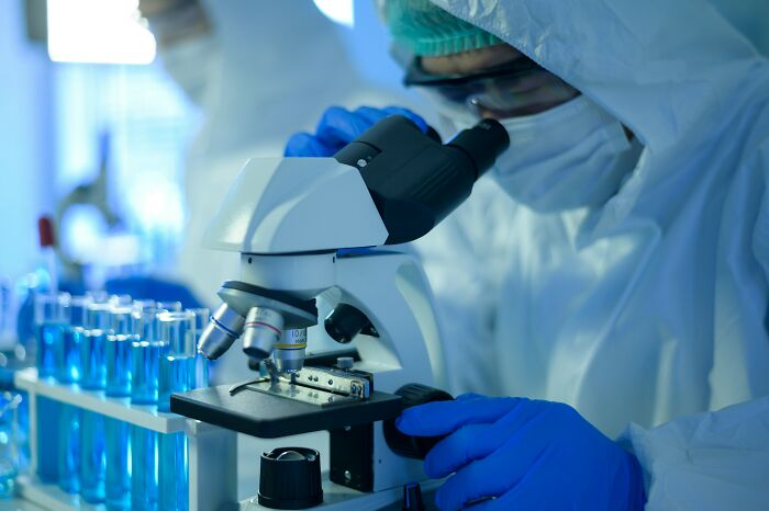 Scientist in protective gear examines samples using a microscope in a lab exploring disturbing science facts.