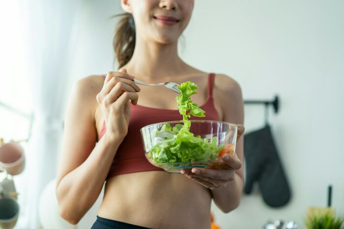 Woman in workout clothes eating a healthy salad indoors illustrating everyday things more dangerous for your health