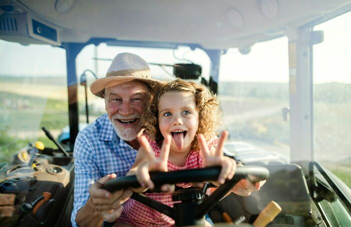 Elderly man and young girl driving tractor together, demonstrating incredible minds without a degree being geniuses.